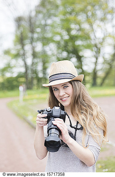 Portrait of smiling young woman comparing two different cameras outdoors