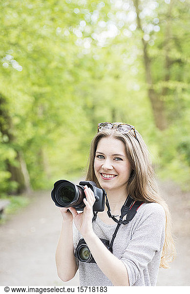 Portrait of smiling young woman comparing two different cameras outdoors
