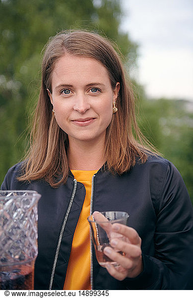 Portrait of smiling young woman holding drink during party on terrace