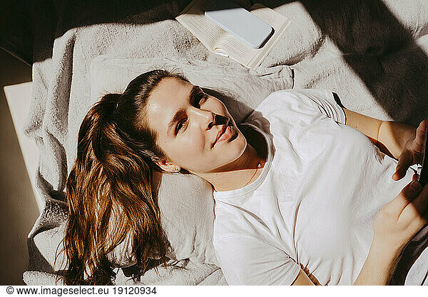 Portrait of smiling young woman lying on bed at home