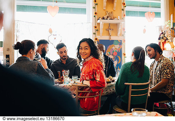 Portrait of smiling young woman sitting amidst multi-ethnic friends during brunch party in restaurant
