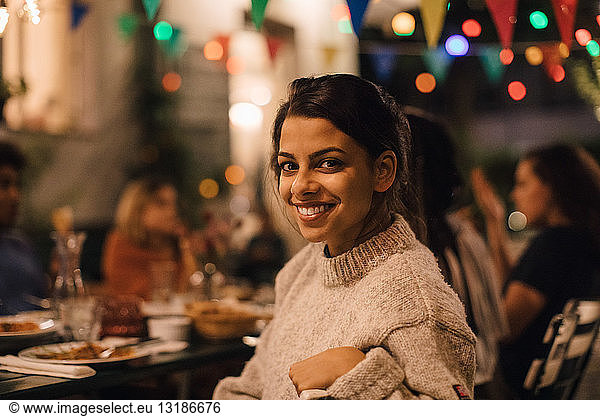 Portrait of smiling young woman sitting at table during dinner party in backyard
