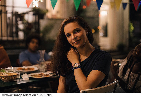 Portrait of smiling young woman sitting on chair by table during dinner party in backyard