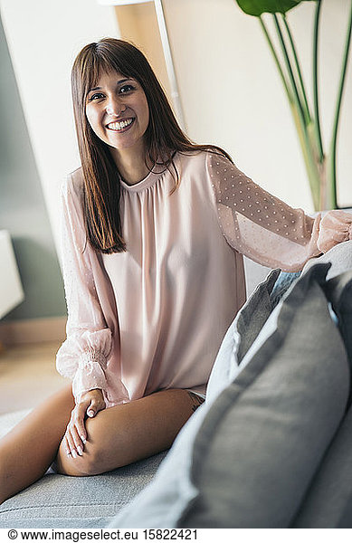Portrait of smiling young woman sitting on couch at home