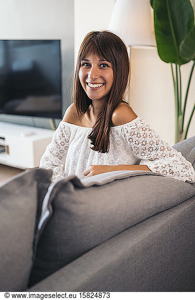 Portrait of smiling young woman sitting on the couch at home