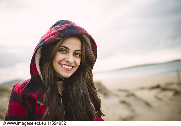 Portrait of smiling young woman wearing hooded jacket on the beach