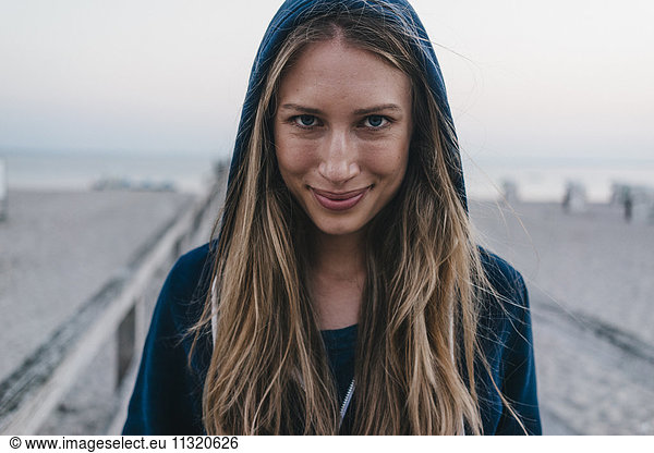 Portrait of smiling young woman wearing hooden jacket standing on jetty