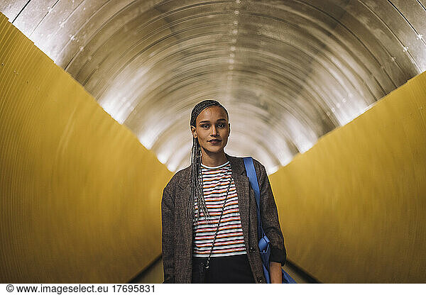 Portrait of smiling young woman with braided hair standing in subway tunnel