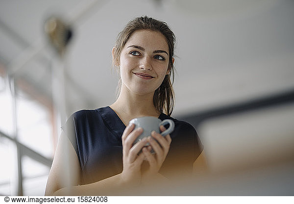 Portrait of smiling young woman with cup of coffee in office