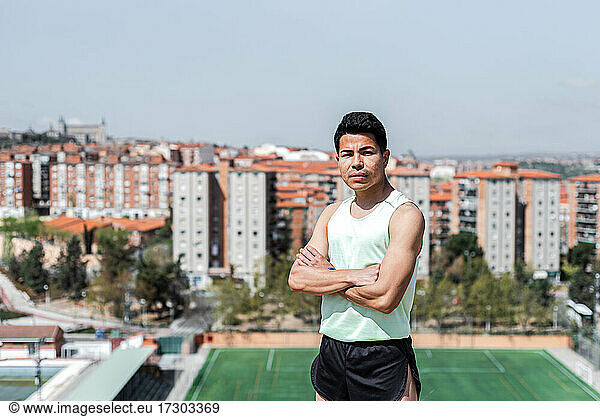 Portrait of South American athlete with arms crossed. Background soccer field and residential buildings. Running concept.