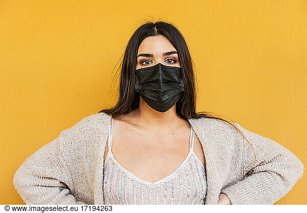 Portrait of Spanish brunette girl with face mask on yellow background wall.