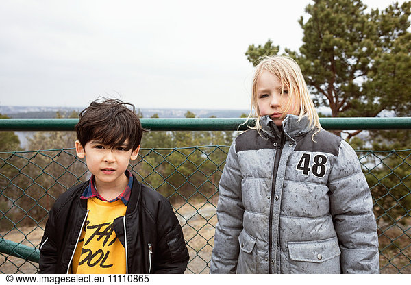 Portrait of students wearing warm clothing standing against fence