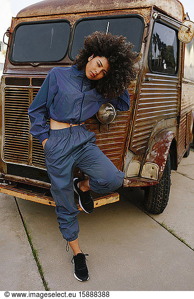 Portrait of stylish young woman wearing tracksuit leaning against old van