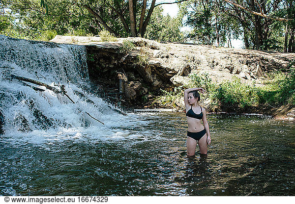 Portrait of teen girl standing in knee deep river near a waterfall