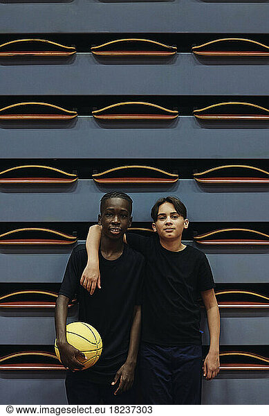 Portrait of teenage boy standing with arm around male friend at sports court