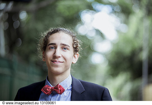 Portrait of teenage boy wearing red bow tie and suit standing outdoors