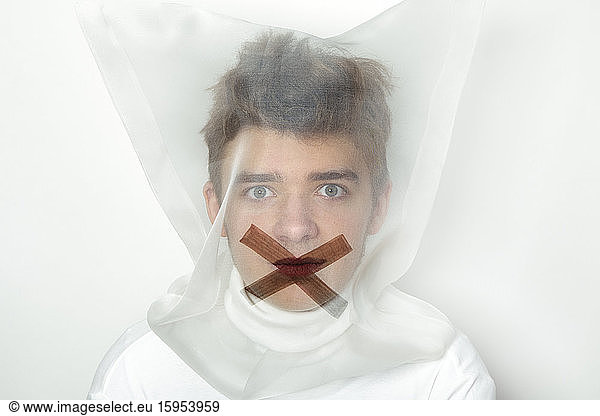Portrait of teenage boy wearing transparent mask with cross on his mouth