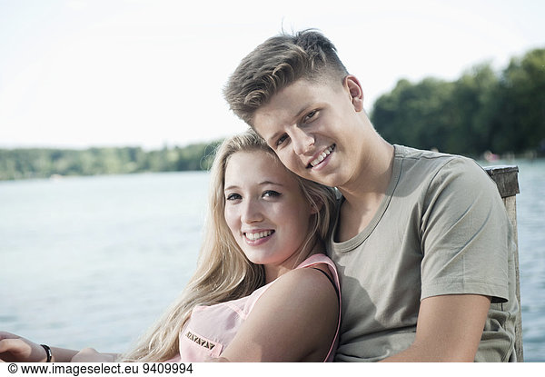 Portrait of teenage couple sitting on a jetty at lake