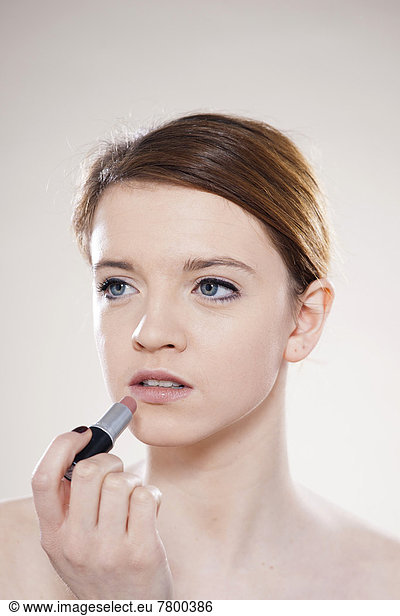 Portrait of Teenage Girl Applying Lipstick in Studio Shot on White Background