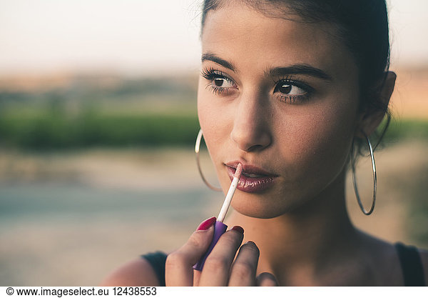 Portrait of teenage girl in nature applying lip gloss