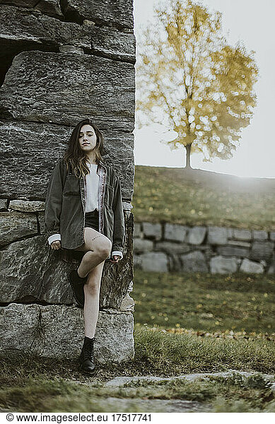 portrait of teenage girl in skirt standing stone wall with tree