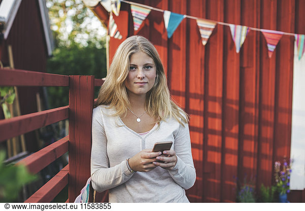 Portrait of teenage girl using mobile phone against house in back yard