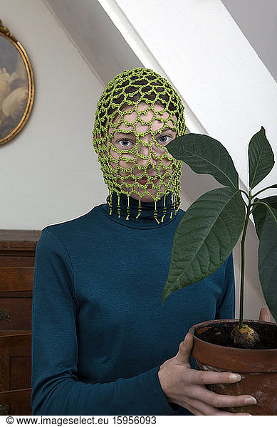 Portrait of teenage girl wearing crocheted green headdress holding potted avocado plant