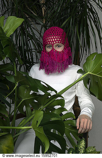 Portrait of teenage girl wearing crocheted pink headdress sitting between house plants