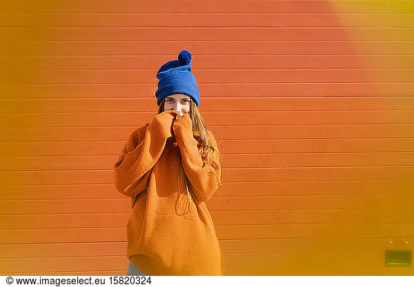 Portrait of teenage girl weraing blue woolly hat and orange sweater in front of orange background