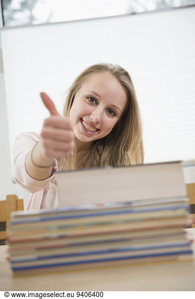 Portrait of teenage girl with books and showing thumbs up  smiling