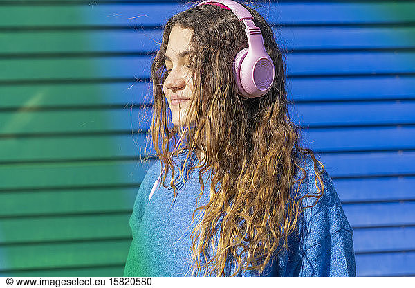 Portrait of teenage girl with eyes closed sky listening music with headphones