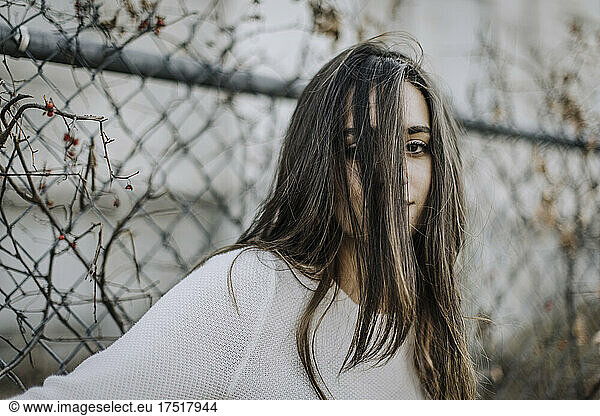 portrait of teenage girl with hair in face against chain link fence