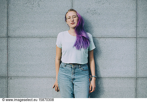 Portrait of teenage girl with purple hair standing against wall
