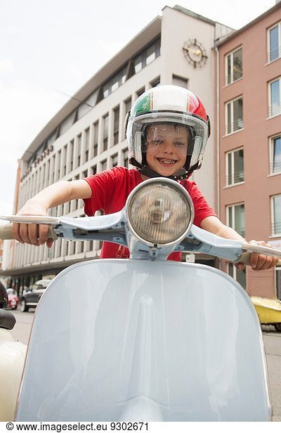 Portrait of ten year old boy pretending to ride motor scooter on city street