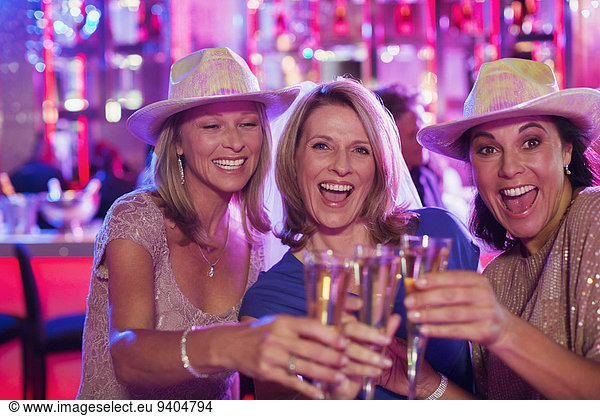 Portrait of three cheerful women wearing cowboy hats toasting with champagne flutes in nightclub