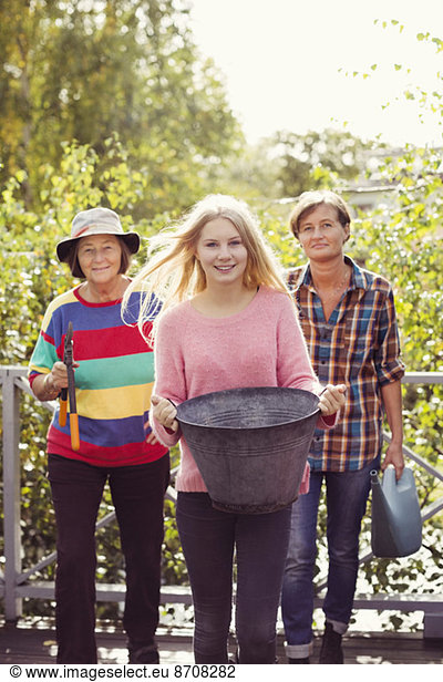 Portrait of three generation females with gardening equipment in yard