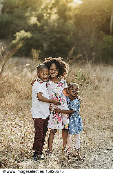 Portrait of three sun-kissed siblings smiling at camera field