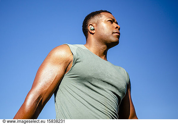 Portrait of top-half of a strong athlete standing against a blue sky