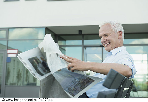 portrait of two business man sitting on a bench reading newspaper
