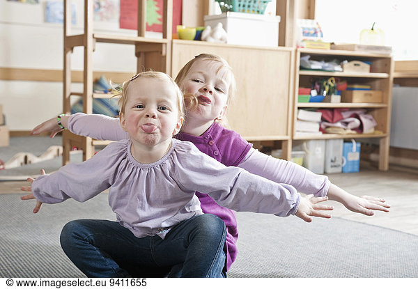 Portrait of two little sisters in kindergarten sticking out tongues