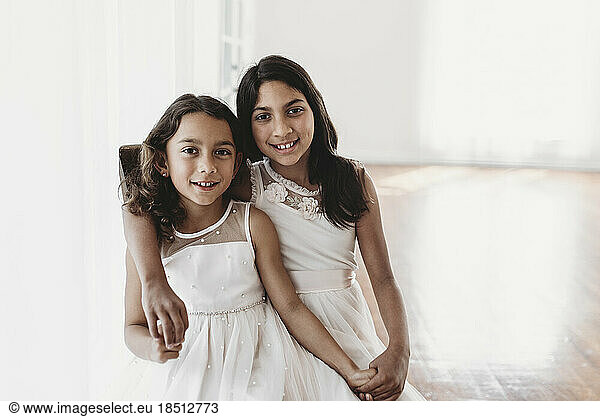 Portrait of two sisters sitting on chair in natural-light studio