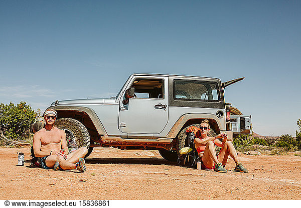 portrait of two straight faced hikers sitting in front of jeep