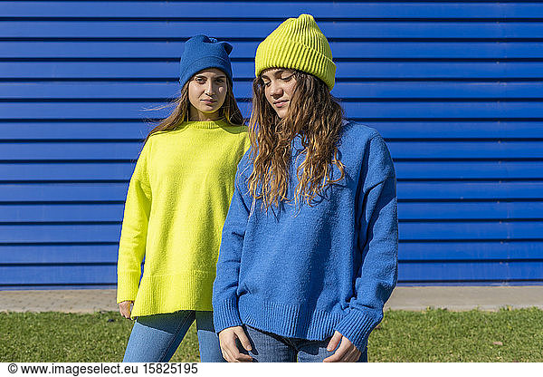 Portrait of two teenage girls wearing matching clothes in front of blue background