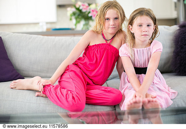 Portrait of two young sisters sitting on sofa