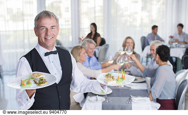 Portrait of waiter holding plate with fancy meals  people at restaurant tables in background