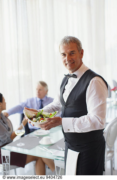 Portrait of waiter holding salad bowl  people at table in background