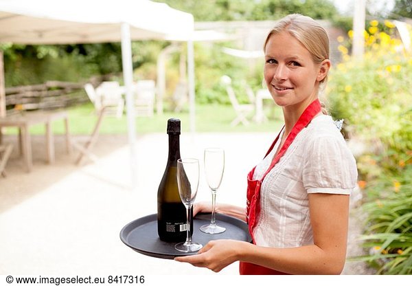 Portrait of waitress with tray of wine and glasses in cafe garden