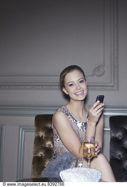 Portrait of well dressed woman drinking champagne and using cell phone