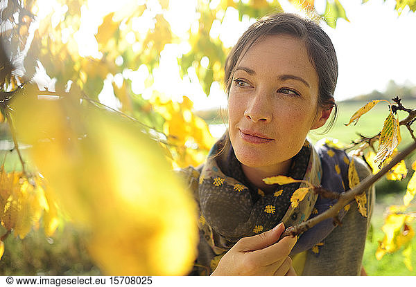 Portrait of woman at twigs with autumn leaves looking at camera