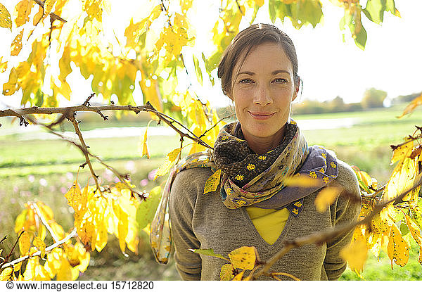 Portrait of woman at twigs with autumn leaves looking at camera